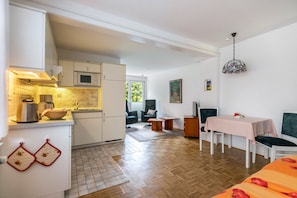 Une cuisine compacte équipée d’un four à micro-ondes, d’une cuisinière et d’un évier. On y trouve également un coin repas avec une table et des chaises, ainsi qu’un espace de vie comprenant un canapé et un fauteuil.
