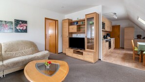 Ein modernes Wohnzimmer mit einer Couch, einem Couchtisch, einem Fernseher, Holzschränken und einer Küchenzeile.