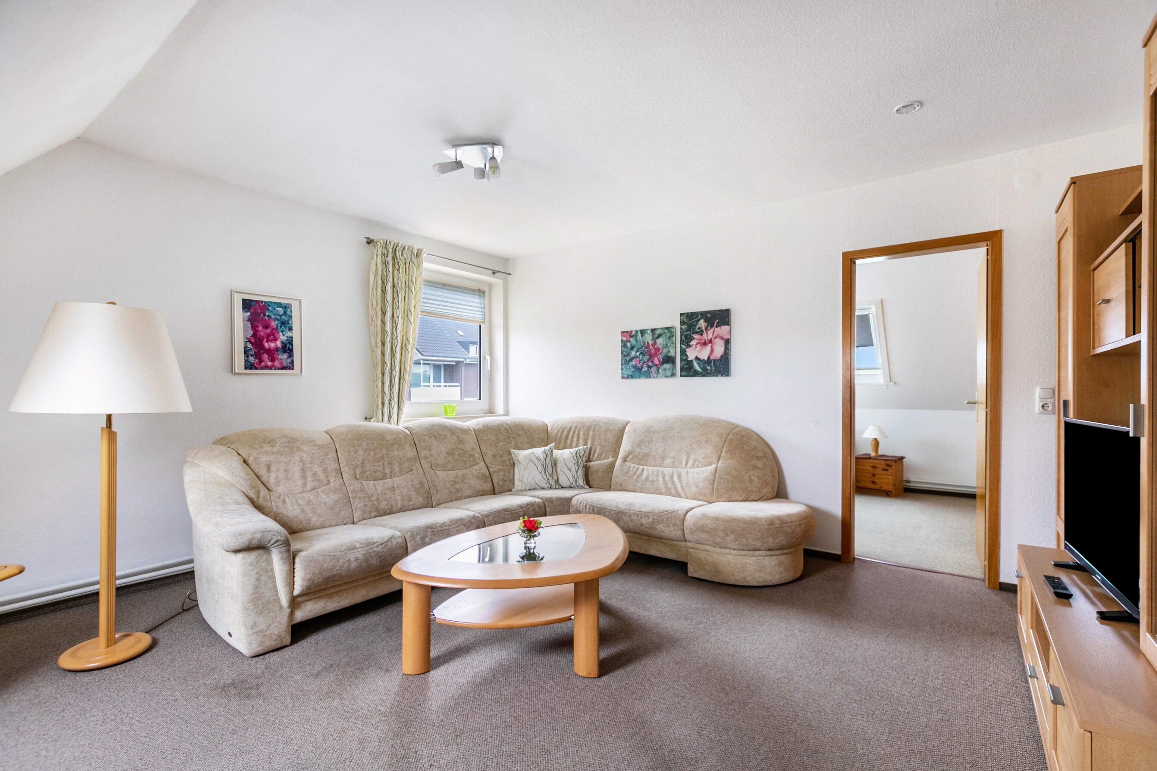 A living room with a beige sectional sofa, a round coffee table, a floor lamp, and a television on a wooden stand.