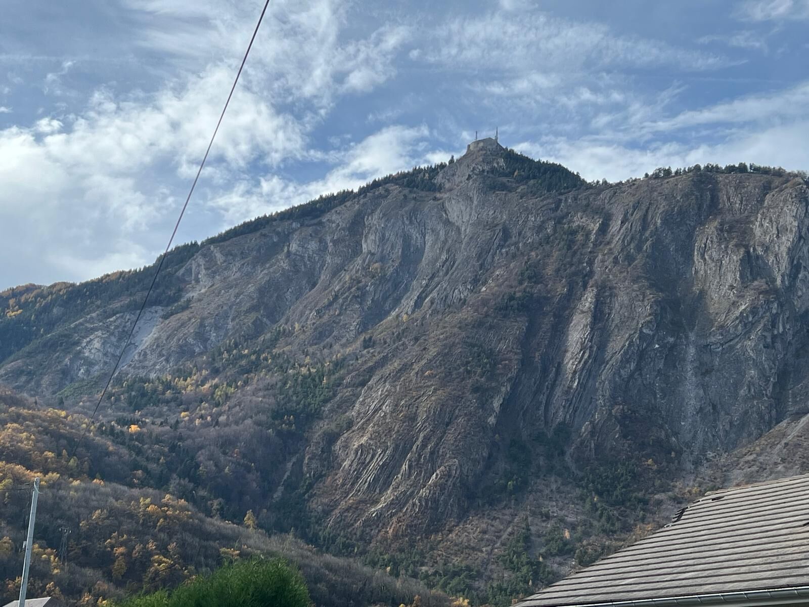 Un paysage montagneux avec un sommet rocheux imposant et un bâtiment doté d’un toit en pente à la base.