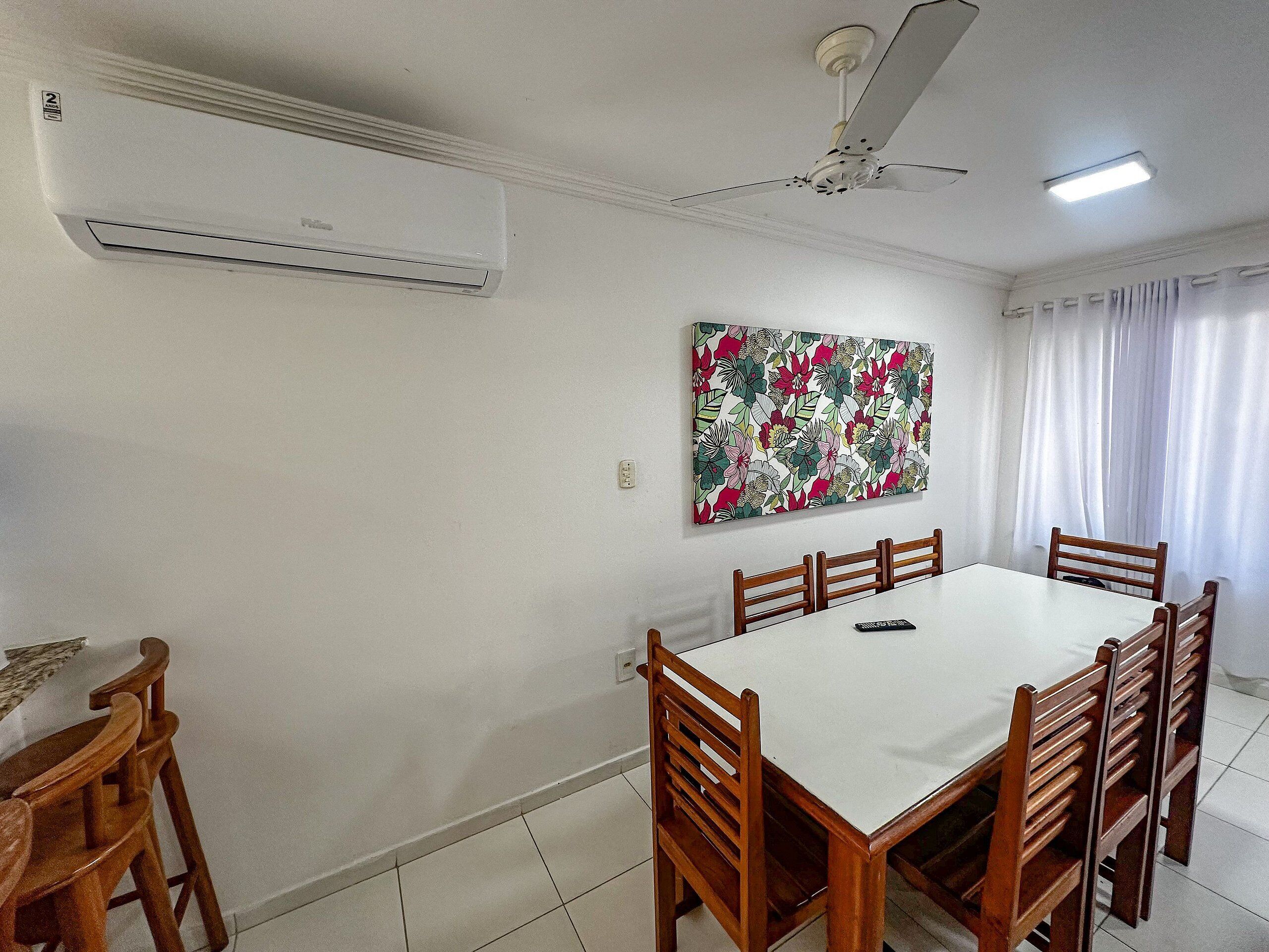 A dining area with a white table and wooden chairs, a ceiling fan, and an air conditioning unit.