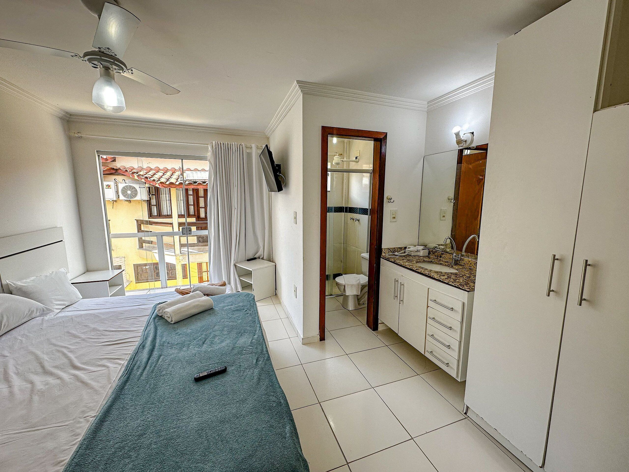 A hotel room with a bed, a bathroom with a mirror and sink, and a view of the outside balcony.