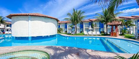 A swimming pool with a circular section, palm trees, and a building with a tiled roof.
