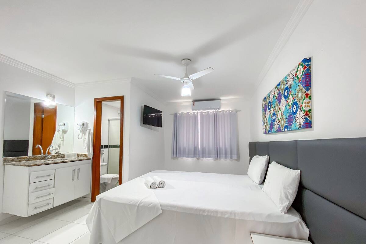 Quarto de hotel com cama, banheiro, televisão e ventoinha no teto.