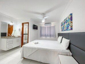 Quarto de hotel com cama, banheiro, televisão e ventoinha no teto.