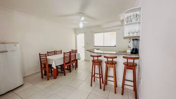 A kitchen with a dining table, bar stools, a refrigerator, a ceiling fan, and a window.