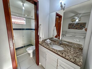 Um banheiro com chuveiro, vaso sanitário, pia e um espelho grande.