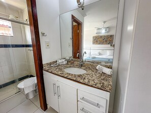 Un baño con lavamanos de encimera de granito, un espejo, toallero y zona de ducha.