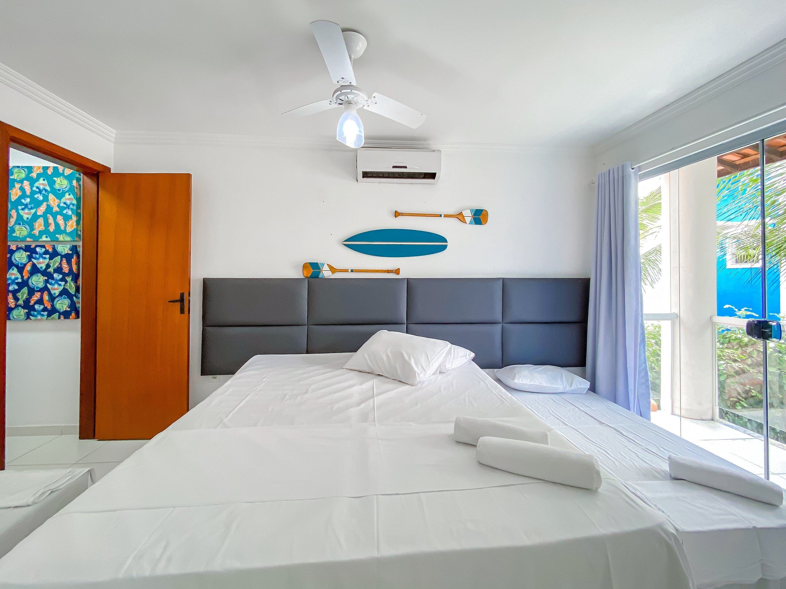 A hotel room with a bed, a ceiling fan, an air conditioning unit, and a view of the outdoors.