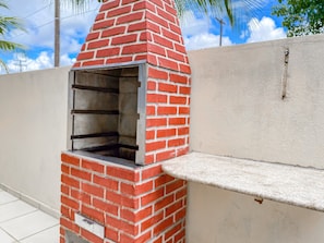 Een buitenbarbecue van baksteen met een metalen deur, geplaatst tegen een muur met een witte afwerking.