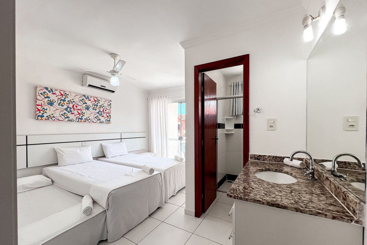Una habitación de hotel con dos camas, un baño con lavamanos y espejo, y un ventilador de techo.