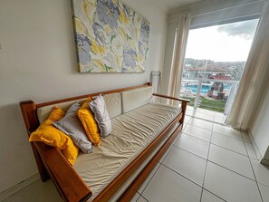 Una habitación con sofá cama de madera, un cuadro abstracto grande en la pared y vistas a una piscina a través de una puerta de cristal.