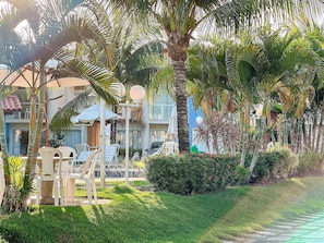 A well-maintained garden with palm trees, a seating area with chairs, and a pathway. - Residencial Mont Sião 1 e 2 (Porto Seguro)