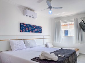 Hotelkamer met een bed, een plafondventilator, een airconditioner, een raam met gordijnen en een kunstwerk aan de muur.