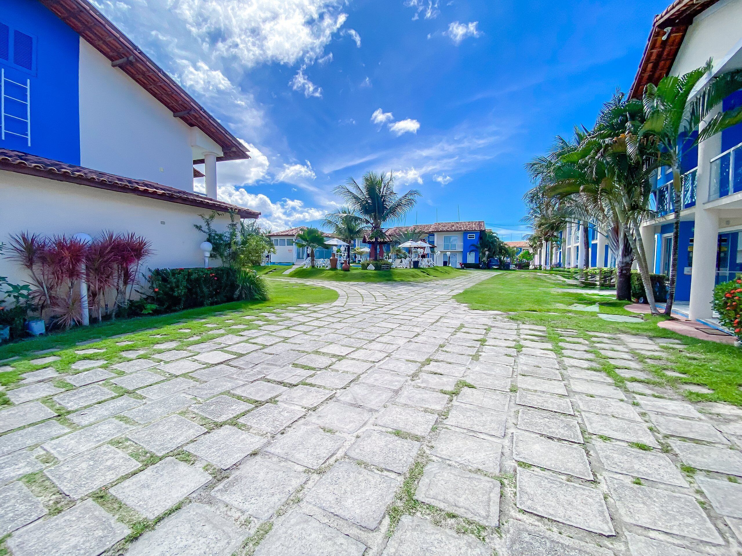 A courtyard with stone pathways, blue and white buildings, and palm trees.