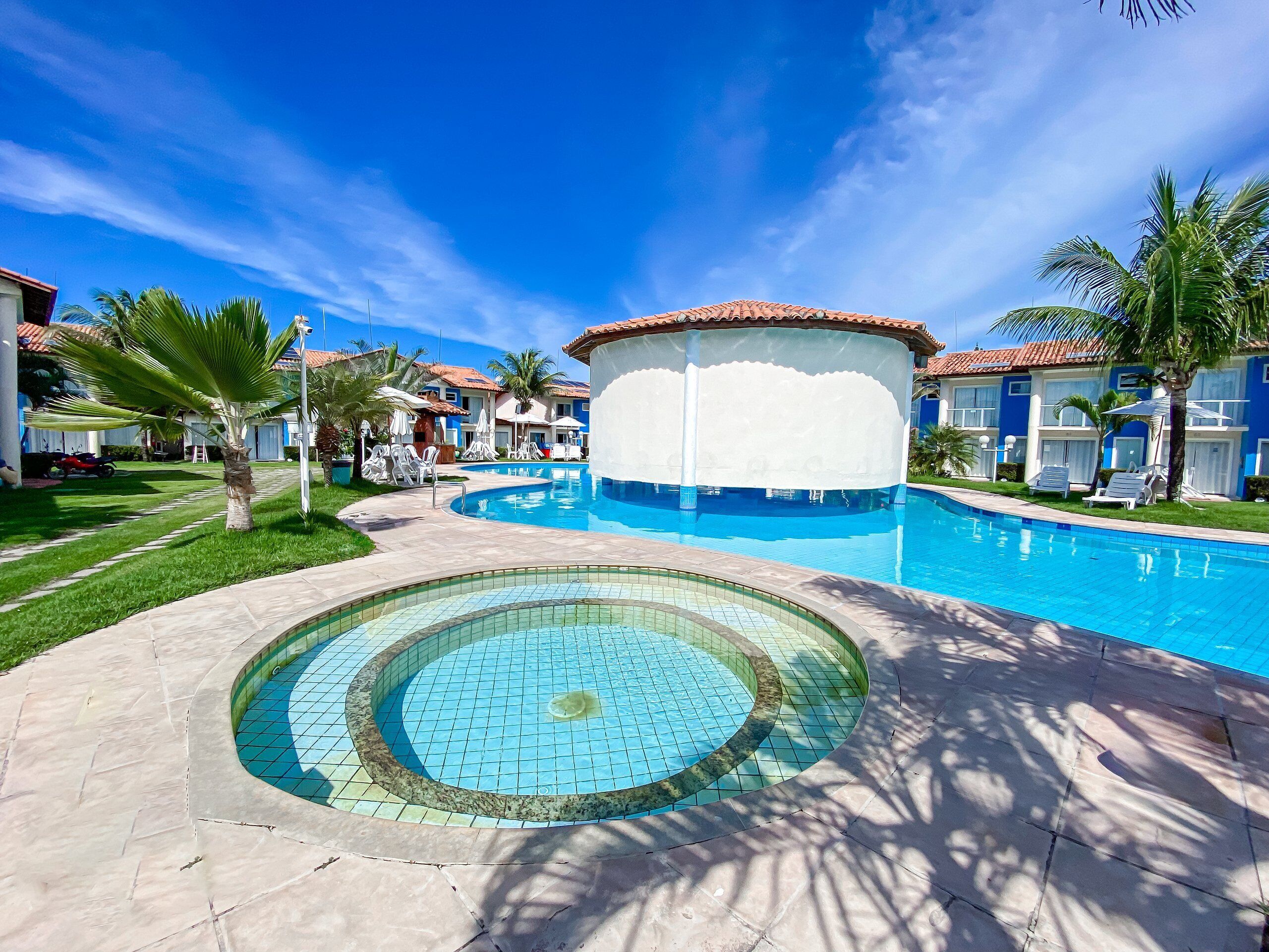 A swimming pool with a circular design, surrounded by palm trees and a clear blue sky.