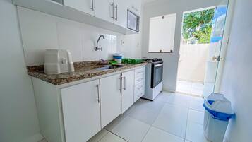 A kitchen with white cabinets, a countertop, a sink, a stove, and a trash bin.