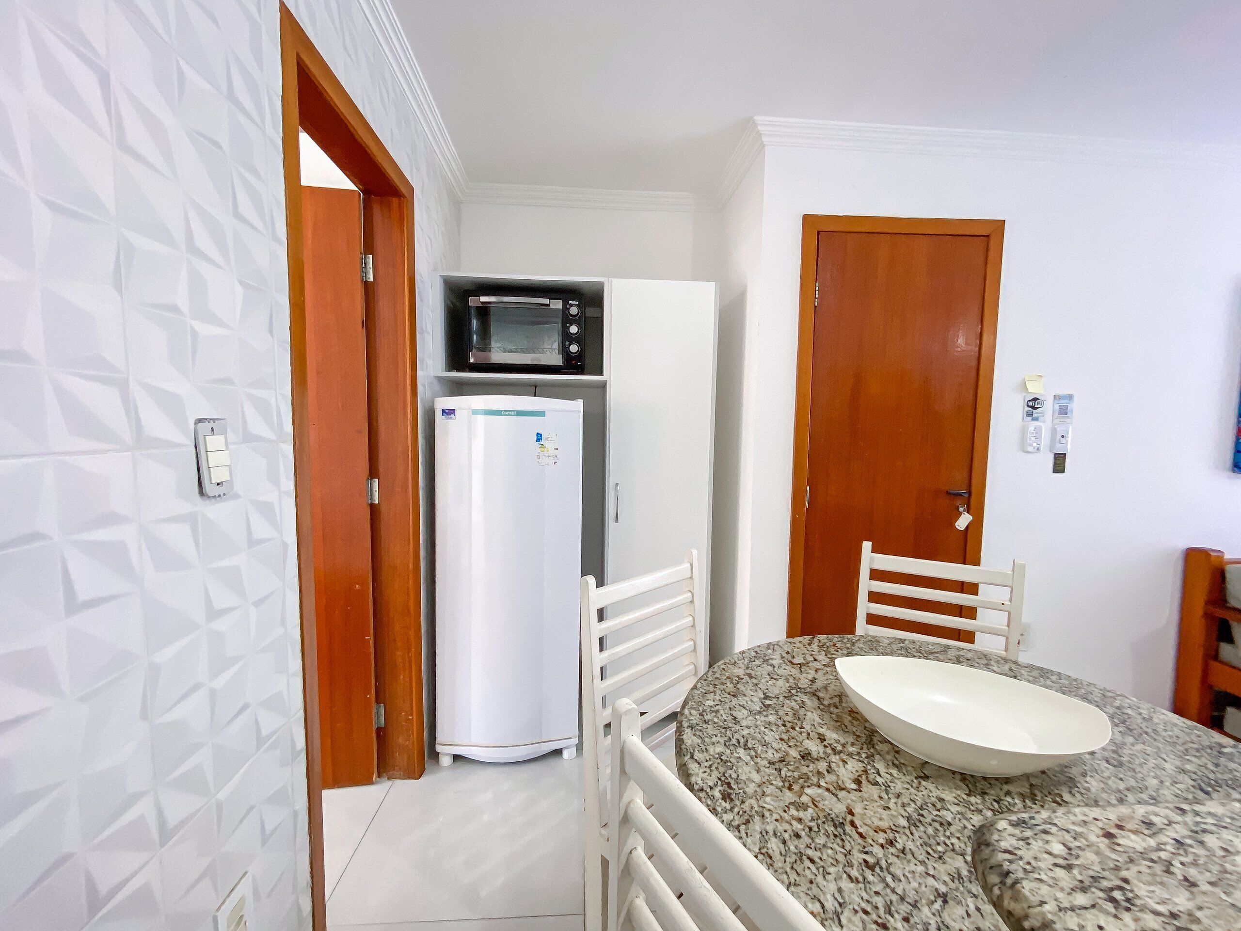 A compact kitchen with a microwave, refrigerator, and a dining area with a granite countertop and white chair.