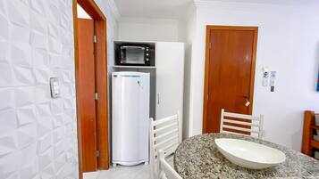 A compact kitchen with a microwave, refrigerator, and a dining area with a granite countertop and white chair.