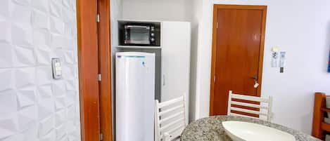 Cocina compacta con microondas, refrigerador y comedor con encimera de granito y silla blanca.