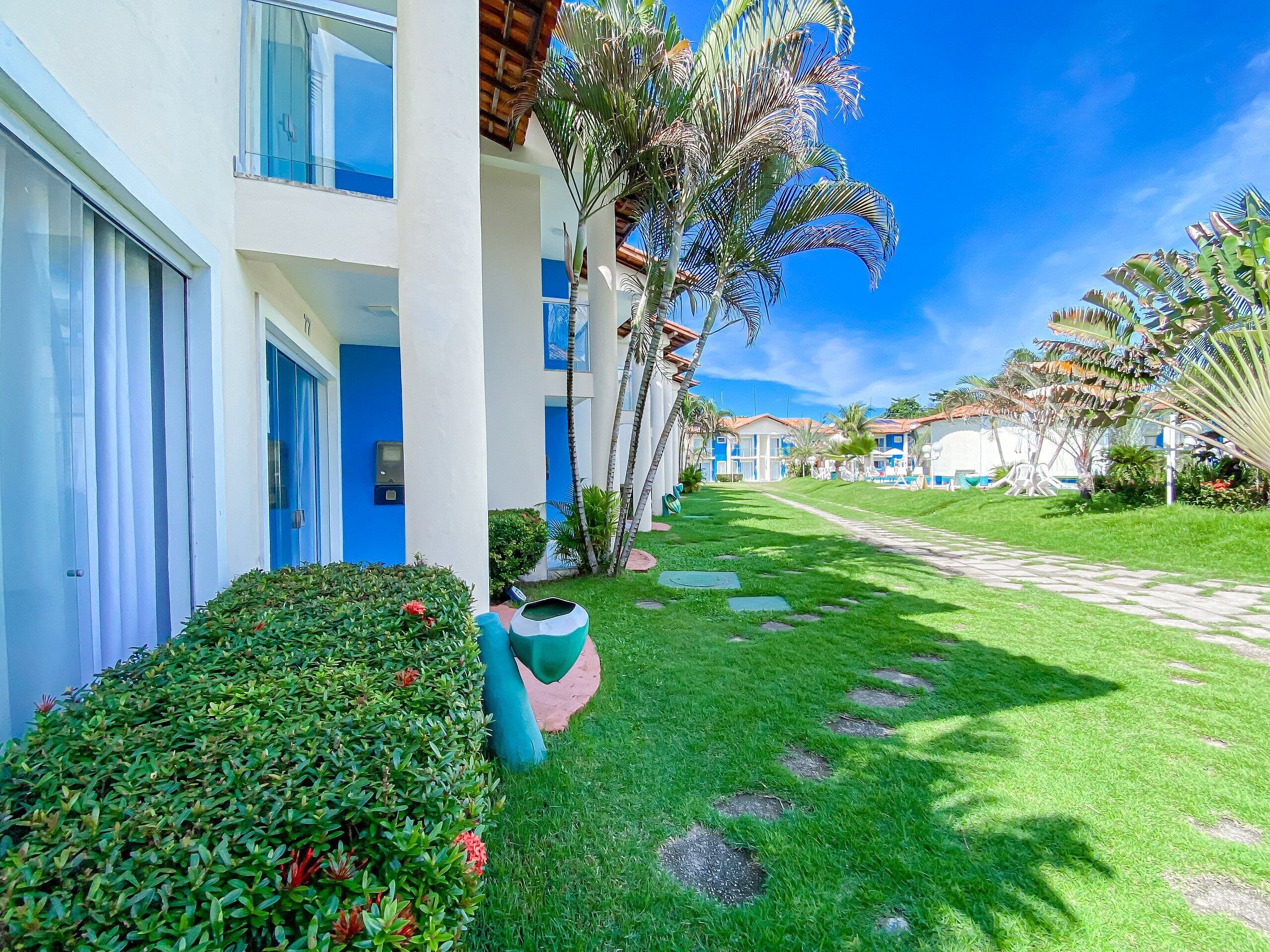 A hotel with a modern design, featuring a well-maintained lawn, palm trees, and a clear blue sky.
