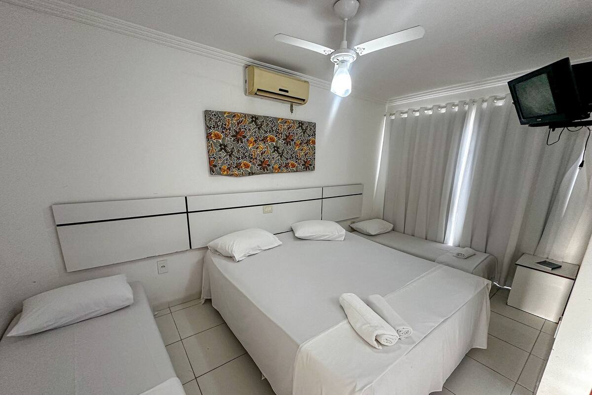 Quarto de hotel com uma cama grande, um ventilador de teto, uma televisão de tela plana e uma obra de arte floral na parede.