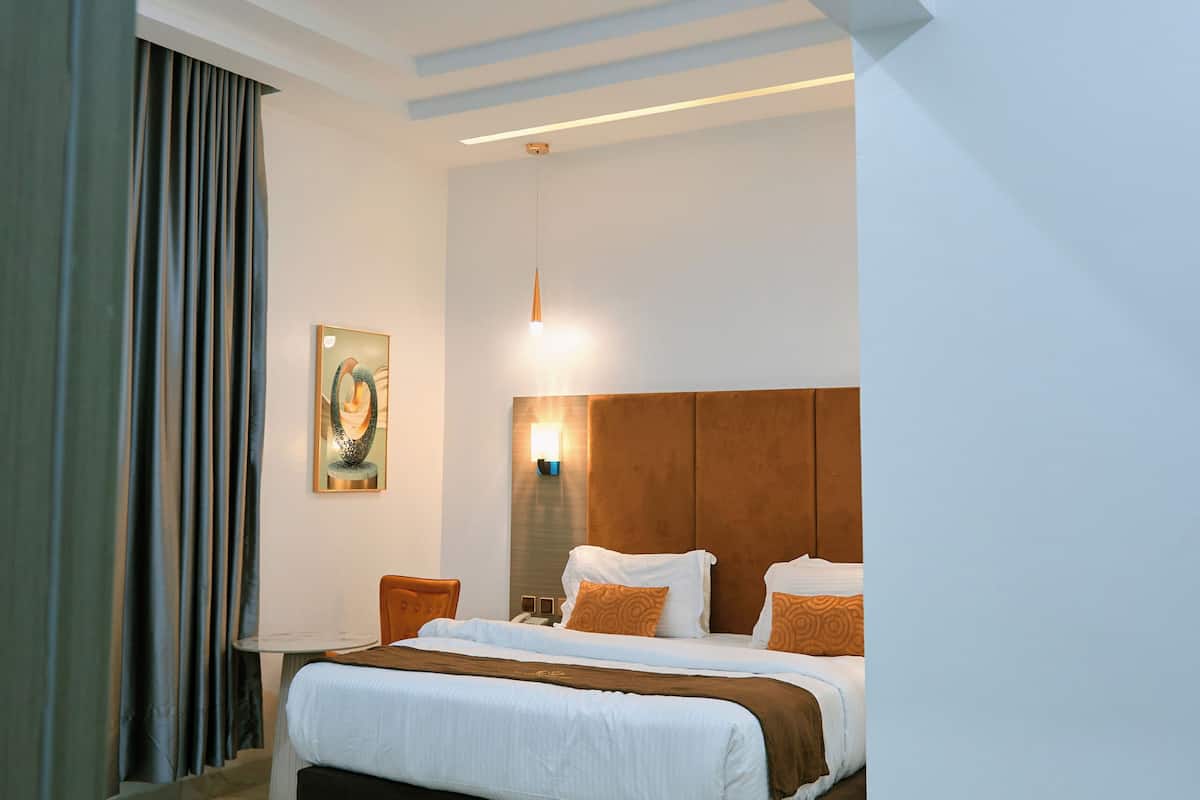 A modern hotel room with a large bed, a desk, and a painting on the wall.