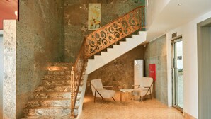 A staircase with ornate metal railings, a stone wall, and a pair of chairs in a lobby area. - Wellington Blu hotel & Suites (Enugu)