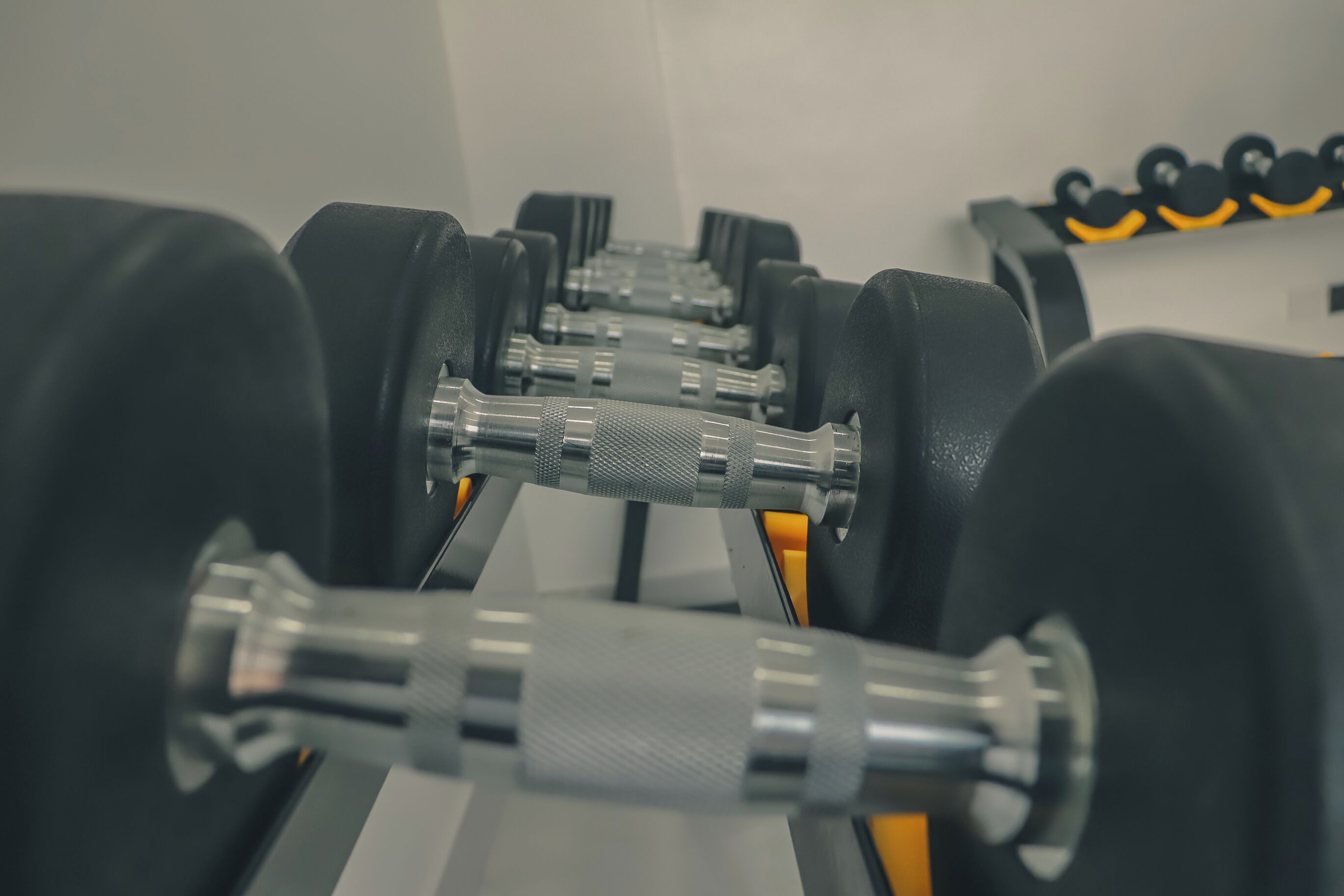 A row of black dumbbells with yellow accents on a rack.