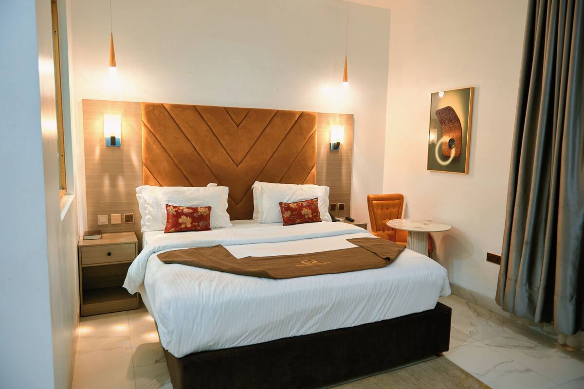 A hotel room with a large bed, two bedside tables, a small round table, and a wall-mounted artwork.