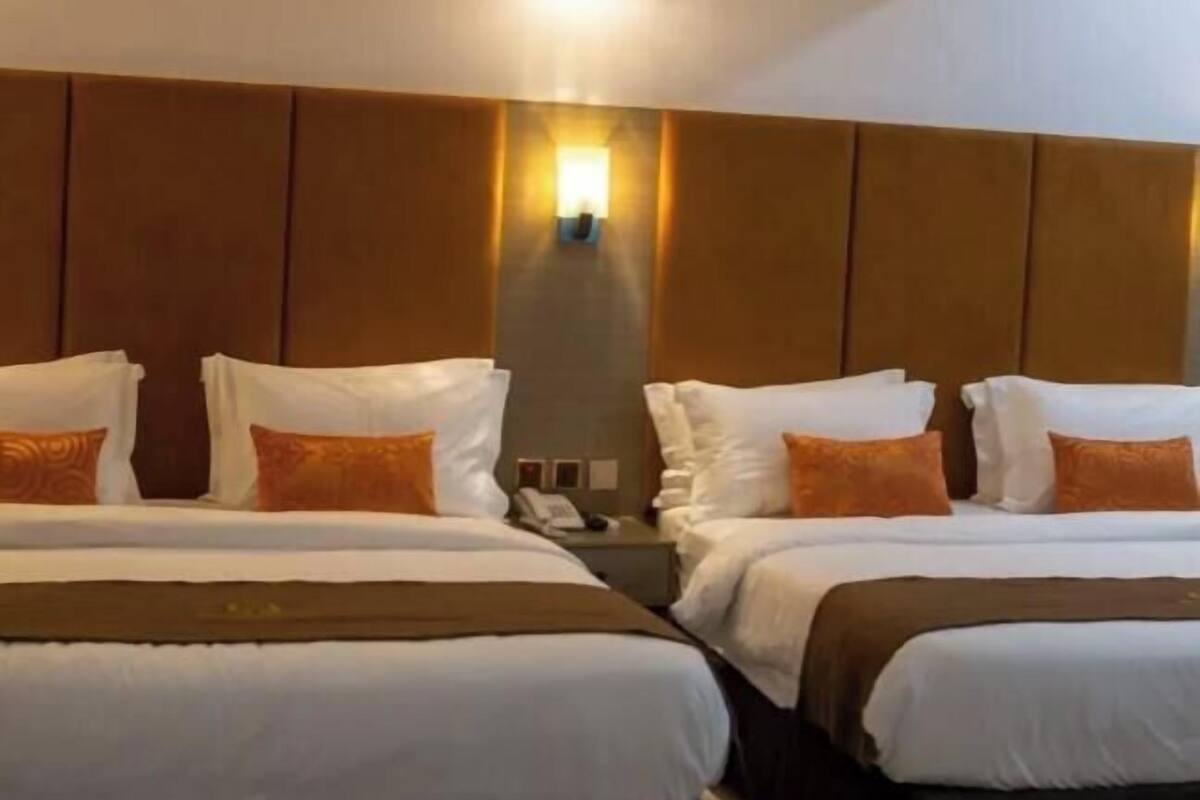 A hotel room with two beds, a wall-mounted light, and a telephone on the nightstand.