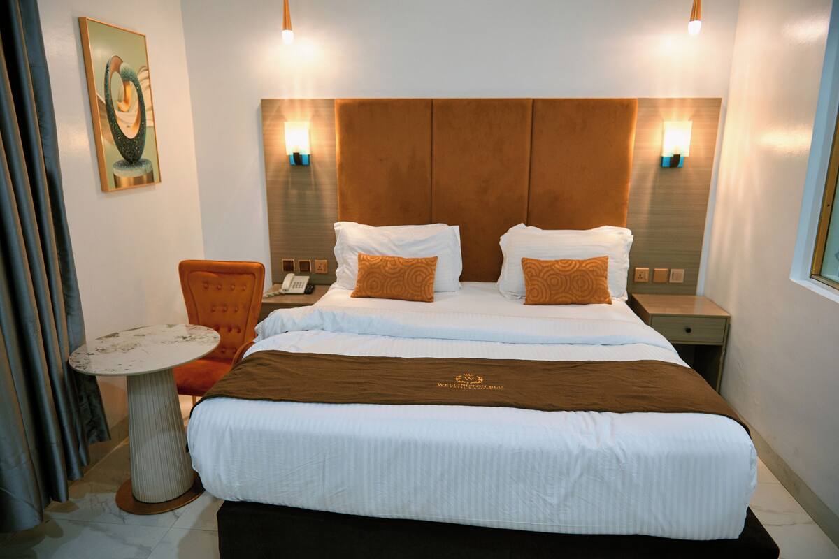 A hotel room with a large bed, two bedside tables, a small round table, and a chair.