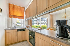 Eine Küche mit Holzausstattung, einem Geschirrspüler, einem Backofen, einem Fenster mit Vorhängen und einer Kaffeemaschine.