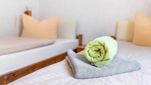 Una cama bien hecha con una toalla enrollada, un cabecero de madera y un cuadro colgado en la pared.