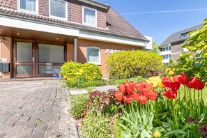 Ein Gebäude mit einem Schild mit der Aufschrift 'PASSAT', einem gepflasterten Eingangsbereich und einem Garten mit rot und gelb blühenden Tulpen.