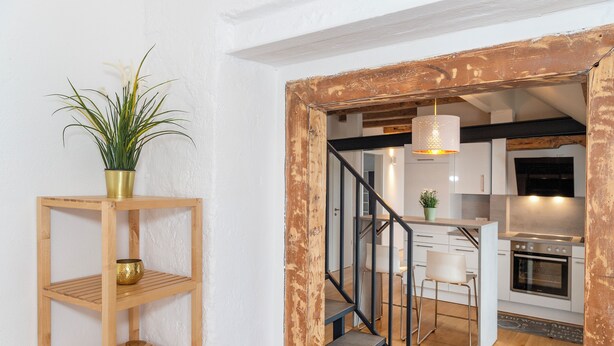 Eine Treppe führt zu einem Küchenbereich mit einem Holzbodenregal und einem Blumentopf.