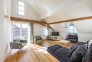 Ein geräumiger Loft mit hohen Decken, freiliegenden Holzbalken, einem großen Fenster und einer modernen Wohnbereich mit Sofa, Fernseher und Sitzgelegenheiten.