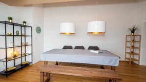 Ein Zimmer mit Holzboden, einem Bett mit gemustertem Überwurf, zwei Pendelleuchten, einer schwarzen Regaleinheit mit Dekorationsobjekten und einem Holznachttisch.