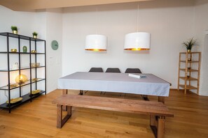 Ein Zimmer mit Holzboden, einem Bett mit gemustertem Überwurf, zwei Pendelleuchten, einer schwarzen Regaleinheit mit Dekorationsobjekten und einem Holznachttisch.