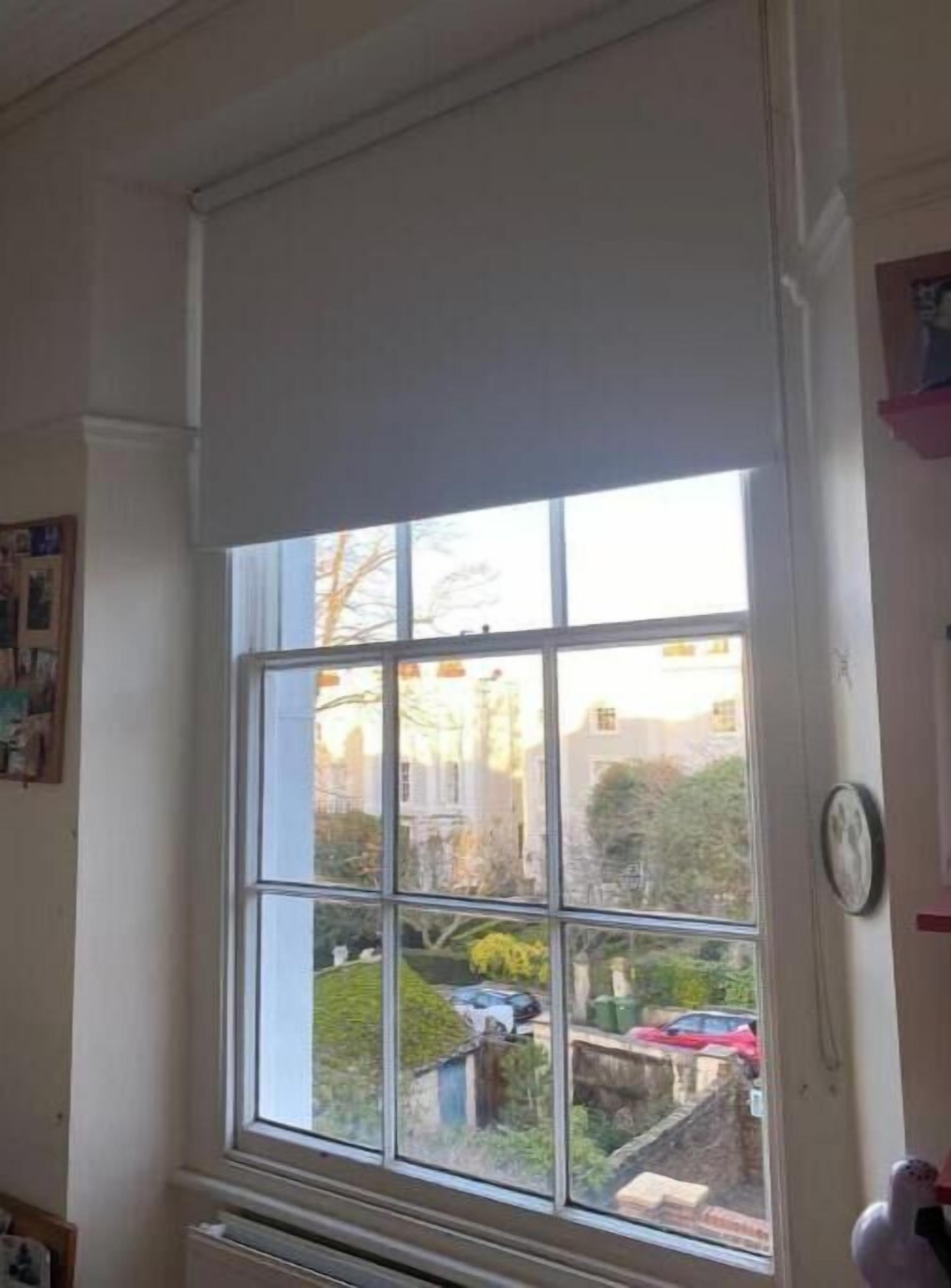 Een kamer met een groot raam, een radiator eronder en een klok aan de muur.