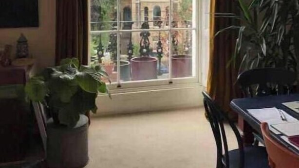 Una habitación con un ventanal grande, una mesa de comedor, sillas, una planta en maceta y un cuadro en la pared.