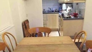 Una mesa de comedor con sillas, una cocina al fondo y una ventana.