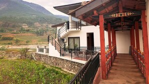 Un edificio con balcón, una escalera y vista a un valle con montañas al fondo.