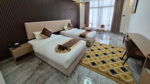 Habitación de hotel con dos camas, un escritorio, una silla, un teléfono y una alfombra estampada.