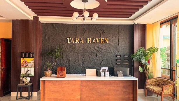 Un mostrador de recepción con una pared de piedra oscura, una zona de espera de madera y una silla a la derecha.