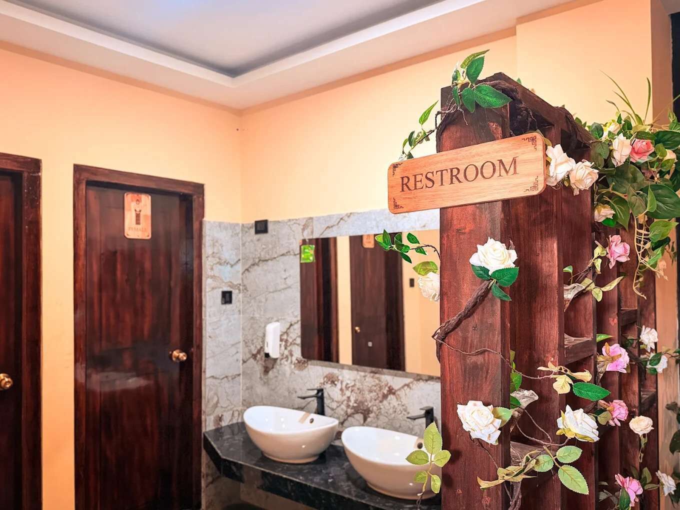 Een toilet met een houten bordje, marmeren wanden en twee wastafels.