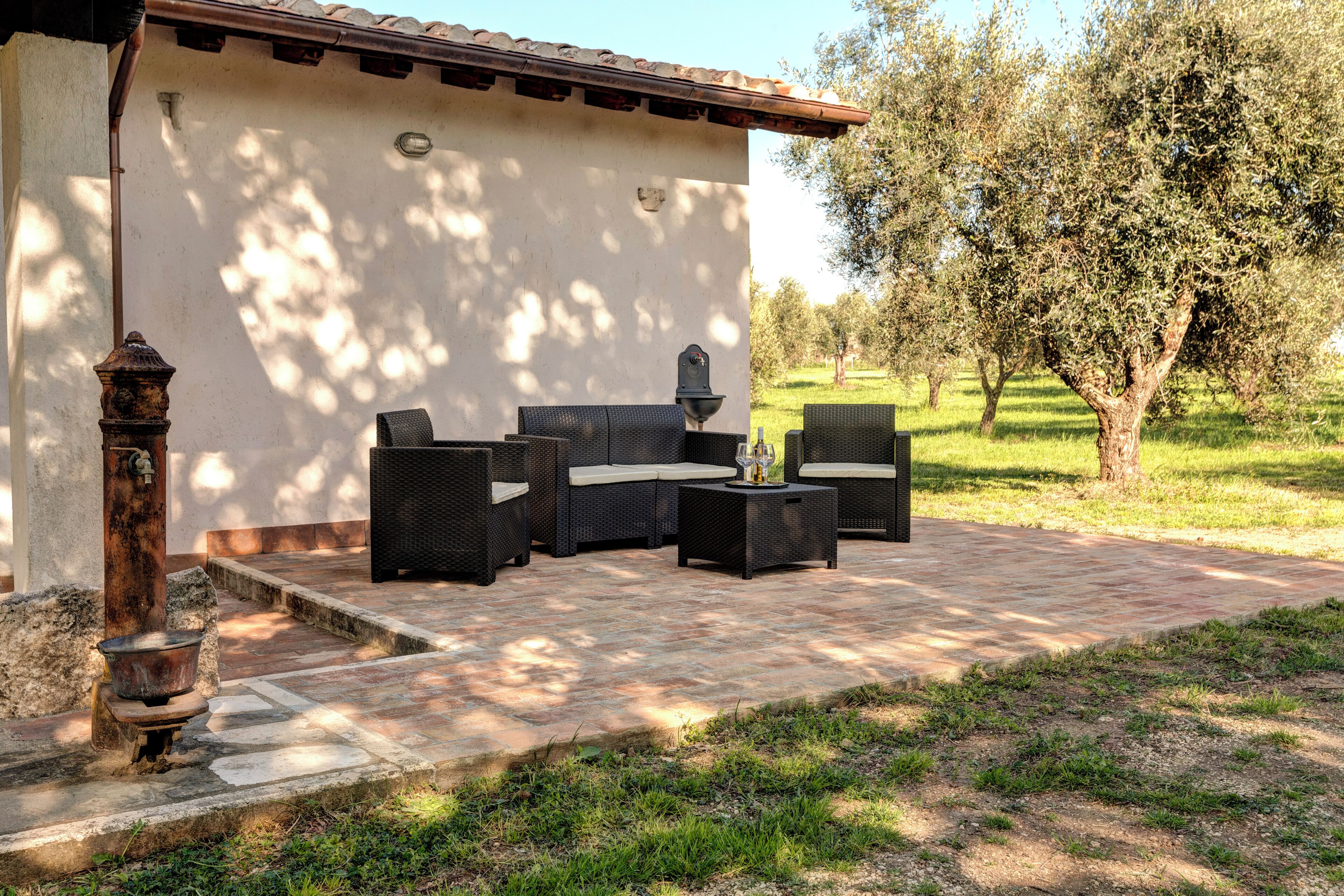 Eine Terrasse im Freien mit Korbmöbeln, einem Steintisch und einem rustikalen Wasserspiel.
