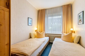Et hotelværelse med to senge, et træskab, en radiator og et vindue med gardiner.