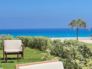 A chair and table on a grassy area with a view of the sea and a palm tree. - Fouka North Coast SA-8A-G03 (Marsa Matrouh)