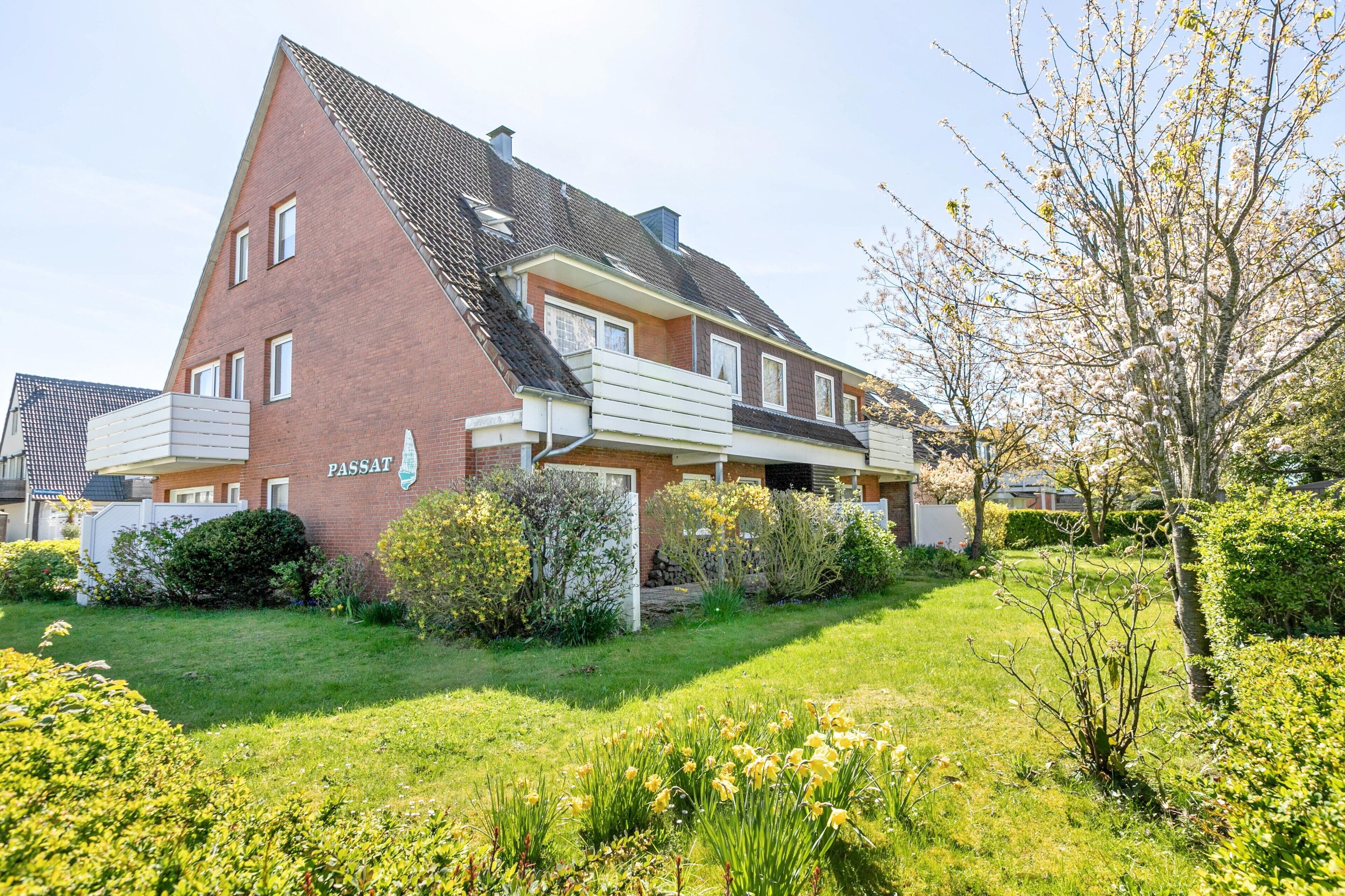 A two-story house with a sloped roof, a visible garage, and a well-maintained garden with flowering plants.